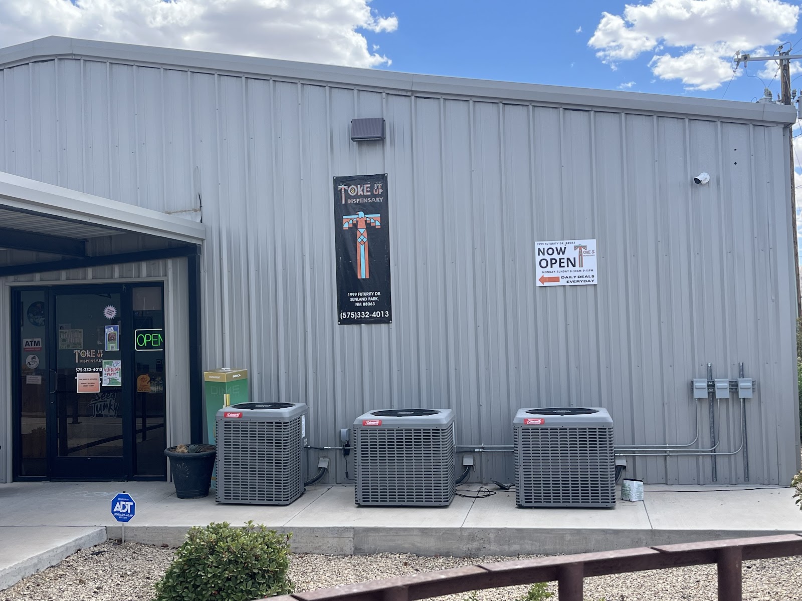 The front of TOKE It Up Dispensary's building on Futurity Drive in Sunland Park, NM: the glass entrance under a metal awning with a green neon OPEN sign, and the shop's banner with its address and phone number.