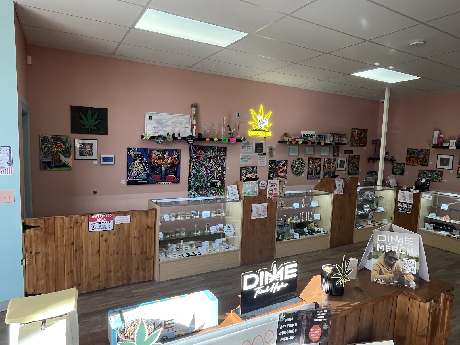 Inside TOKE It Up Dispensary — terracotta walls covered in framed artwork, wooden display cases, and a neon cannabis-leaf sign above the counter.