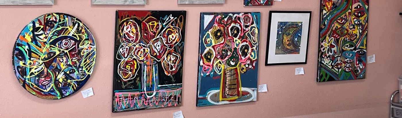 A row of bright, abstract paintings of faces and flowers hung along a rose-pink wall.