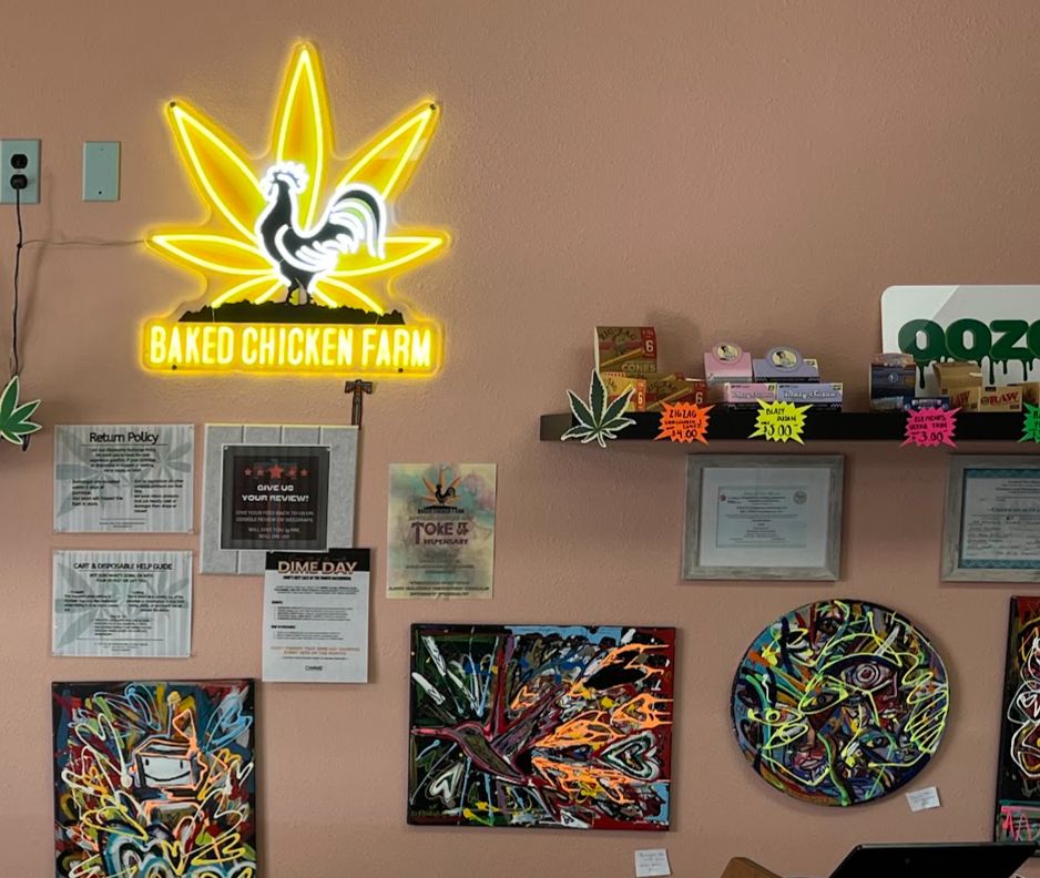 A yellow rooster-and-leaf neon sign glowing above the counter, with framed notices and colourful paintings below it.