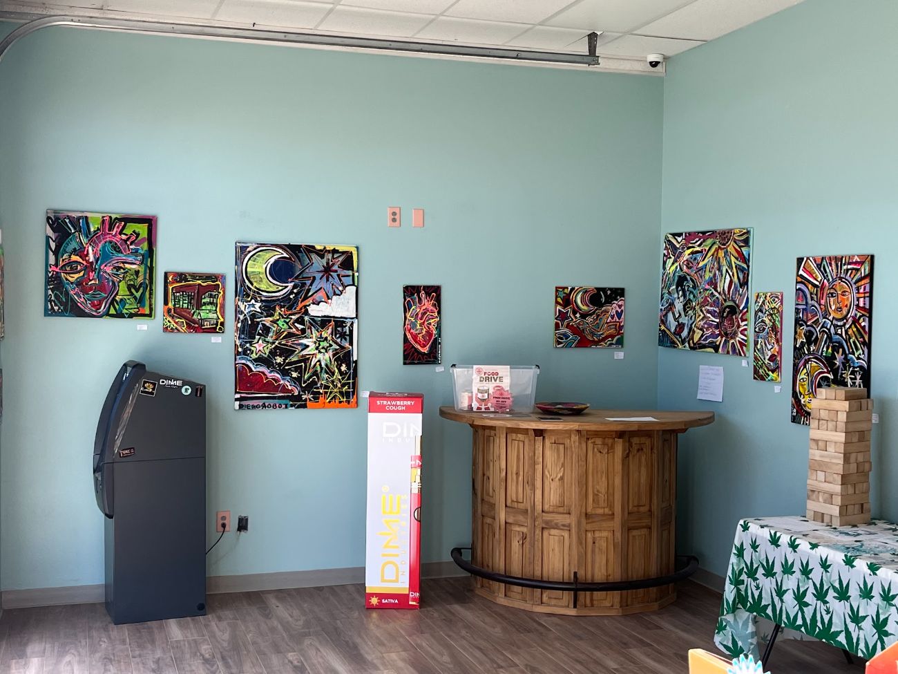 A corner of the mint-green room with a round wooden table, an ATM and more paintings on the walls.
